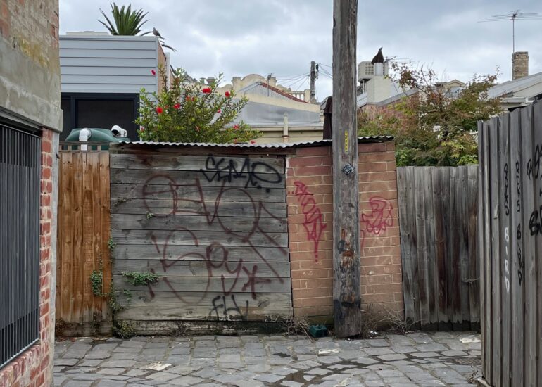 Bluestone laneway ending at a graffitied timber gate and power pole, Melbourne inner north, hidden__north documentary photography