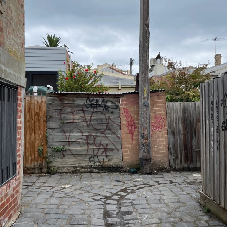 Bluestone laneway ending at a graffitied timber gate and power pole, Melbourne inner north, hidden__north documentary photography