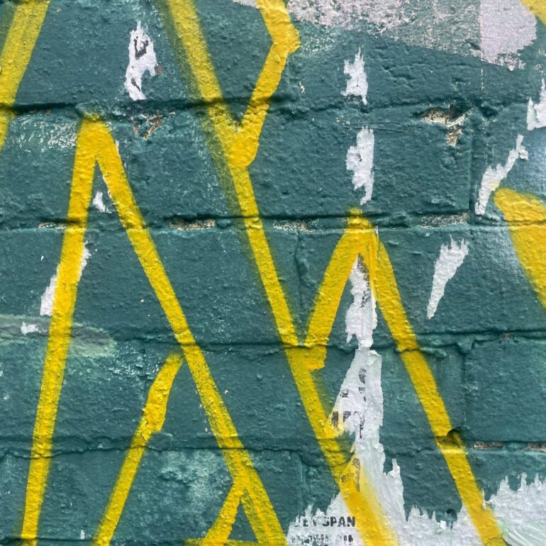 Yellow spray-painted lines over dark green painted brick, Melbourne inner north, hidden__north documentary photography