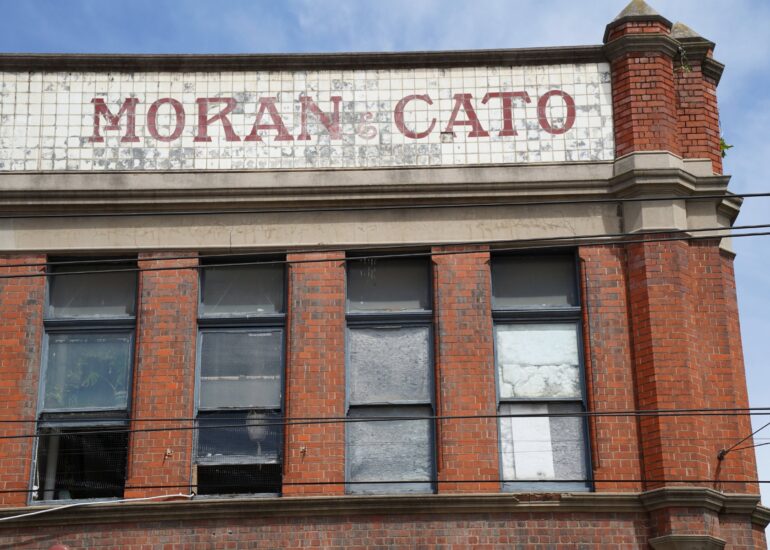 Faded Moran & Cato lettering on a tiled parapet above a red brick corner building, Melbourne inner north, hidden__north documentary photography