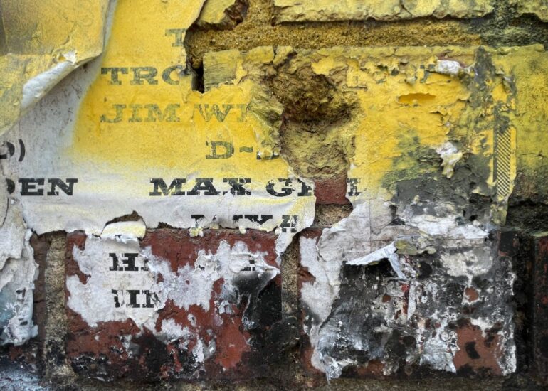 Weathered yellow poster fragments over brick and render, Melbourne inner north, hidden__north documentary photography