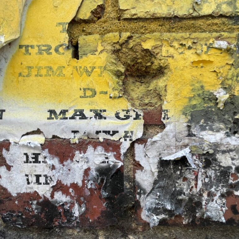 Weathered yellow poster fragments over brick and render, Melbourne inner north, hidden__north documentary photography