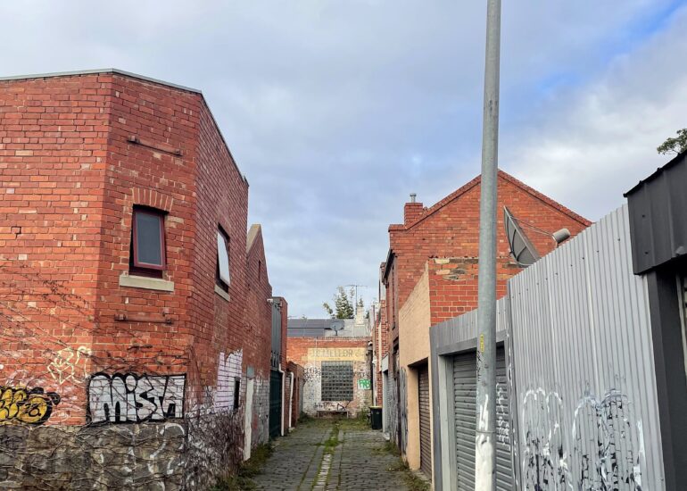 Bluestone laneway curving past a red brick corner building and a street lamp, Melbourne inner north, hidden__north documentary photography