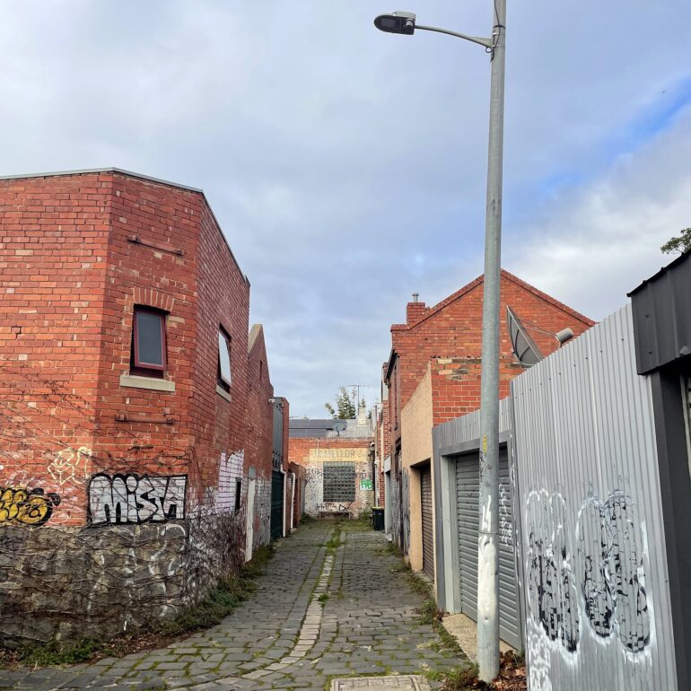 Bluestone laneway curving past a red brick corner building and a street lamp, Melbourne inner north, hidden__north documentary photography