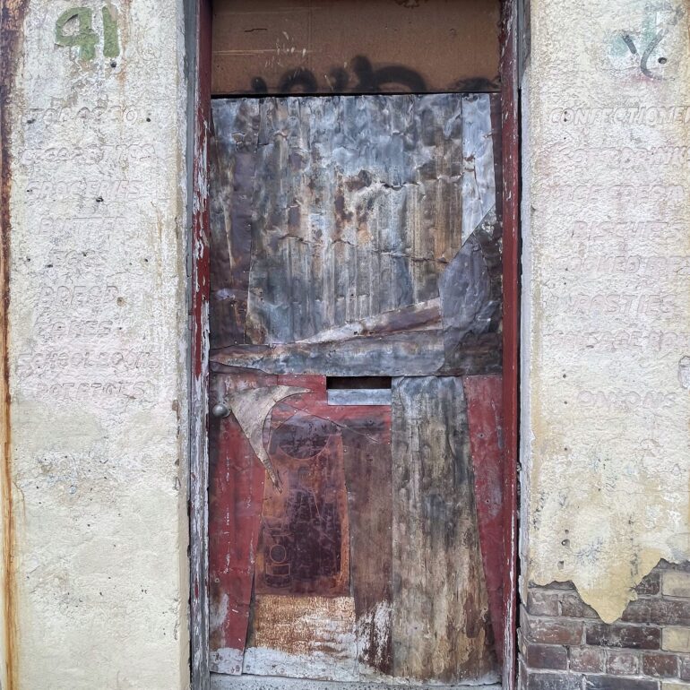 Boarded shopfront door with layered peeling paint and render, Melbourne inner north, hidden__north documentary photography
