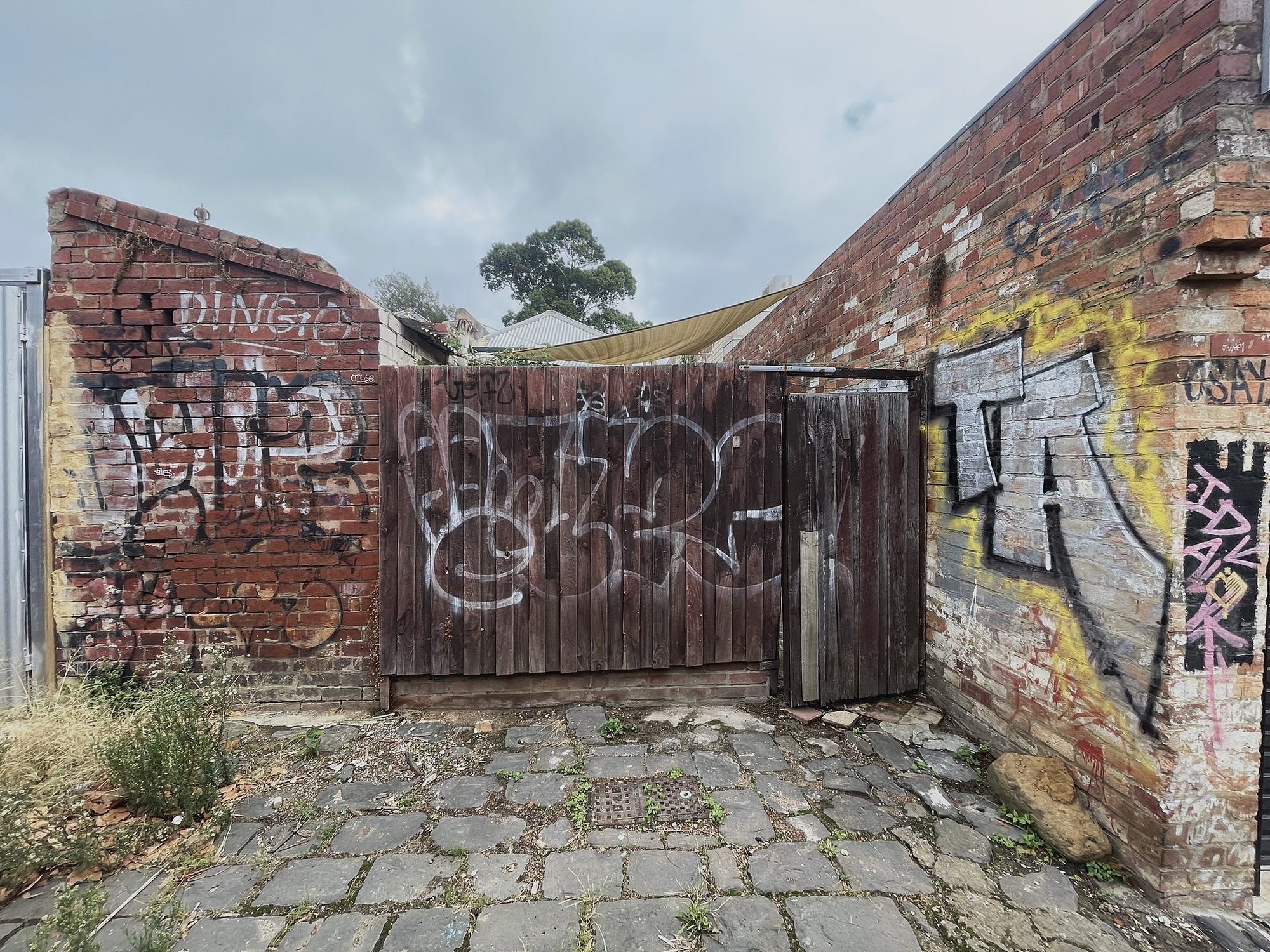 Tagged brick corner and timber gate at the end of a laneway, Melbourne inner north, hidden__north documentary photography