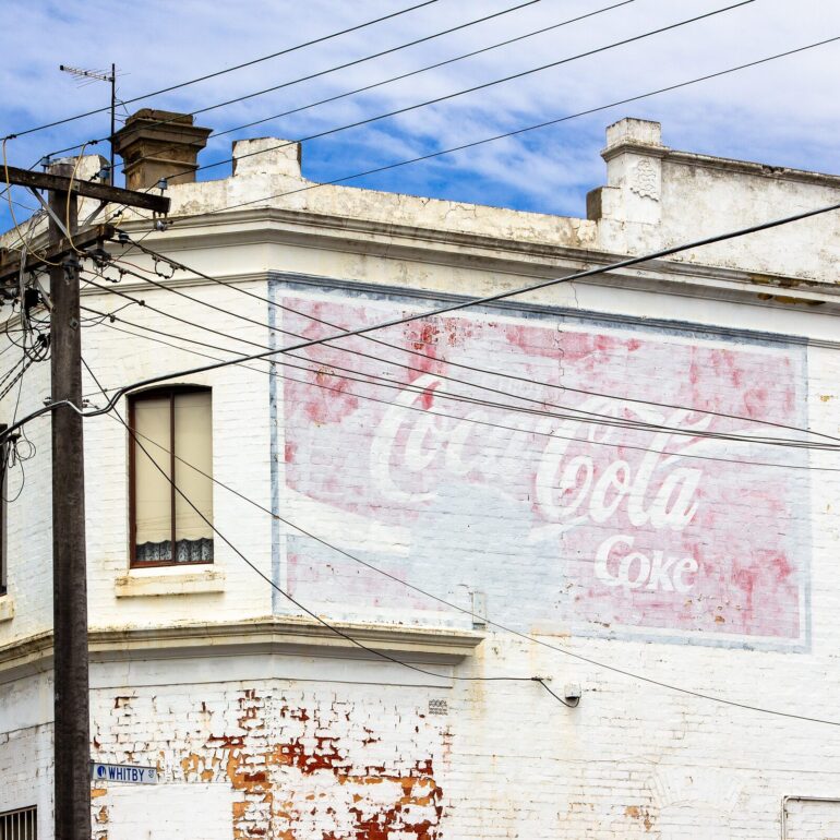 Faded Coca-Cola ghost sign on a white rendered corner building, Whitby Street, Melbourne inner north, hidden__north documentary photography