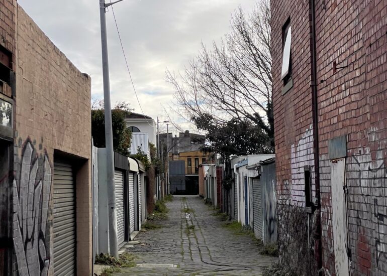 Narrow cobbled laneway lined with garage doors under an overcast sky, Melbourne inner north, hidden__north documentary photography