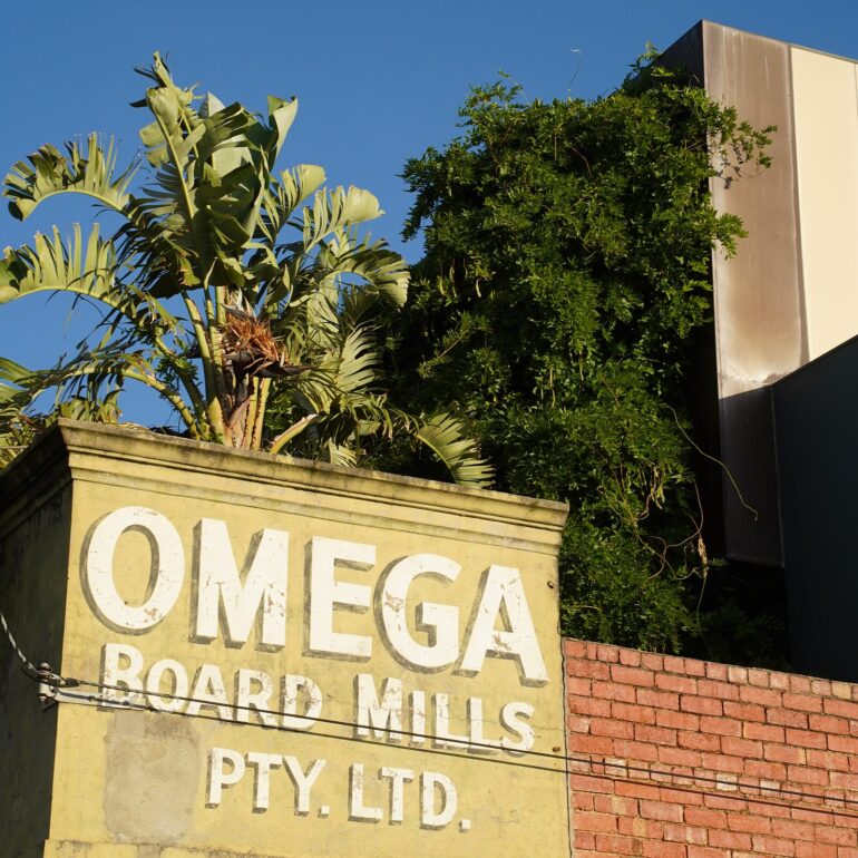 Faded Omega Board Mills ghost sign on a yellow parapet above a red brick wall, Melbourne inner north, hidden__north documentary photography