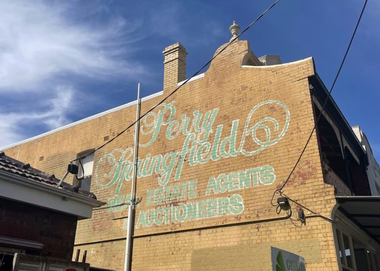 Faded Perry Springfield real estate agents ghost sign in pale green script on a yellow brick gable, Melbourne inner north, hidden__north documentary photography