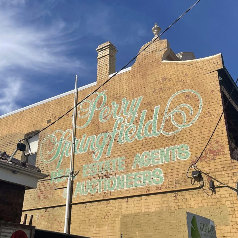 Faded Perry Springfield real estate agents ghost sign in pale green script on a yellow brick gable, Melbourne inner north, hidden__north documentary photography