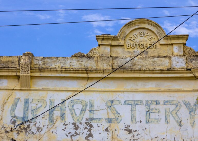 Faded Upholstery lettering below a Butcher pediment on a pale yellow shopfront, Melbourne inner north, hidden__north documentary photography