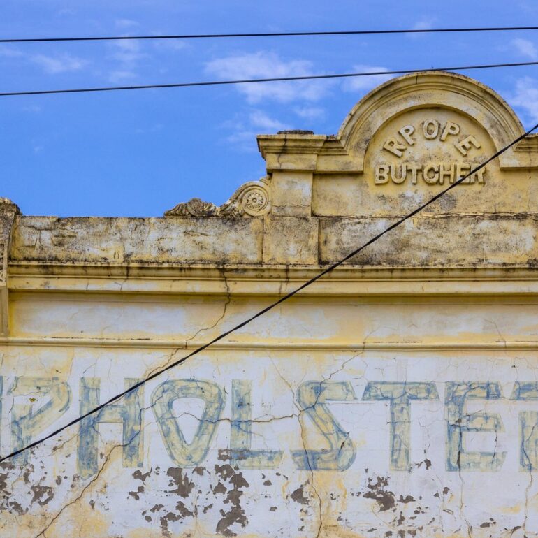 Faded Upholstery lettering below a Butcher pediment on a pale yellow shopfront, Melbourne inner north, hidden__north documentary photography