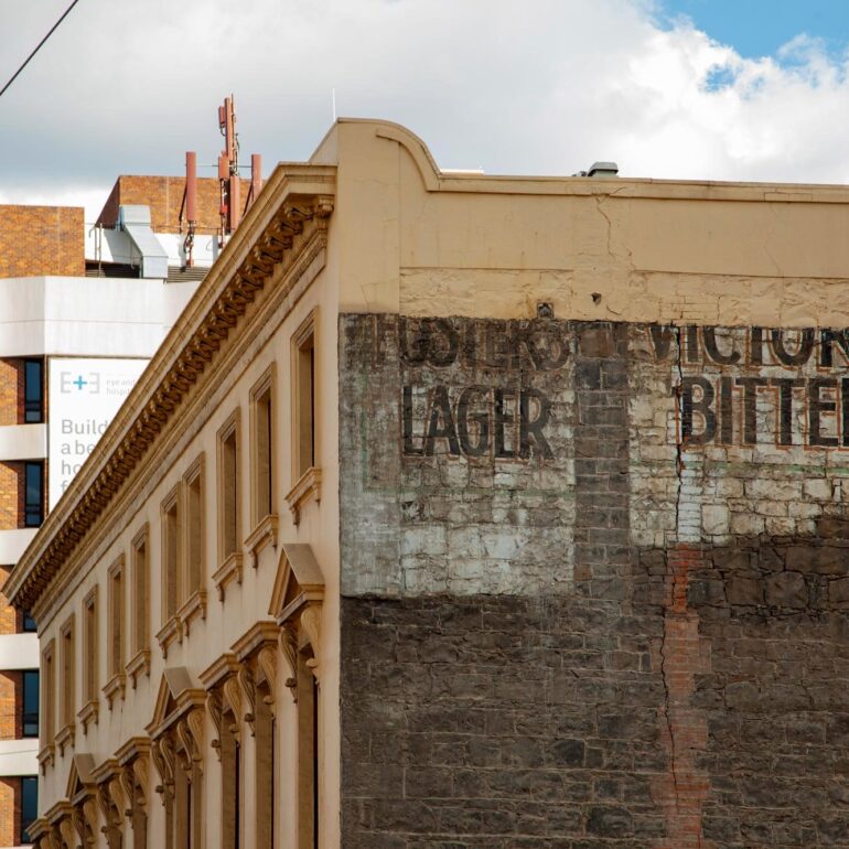 Victoria Bitter ghost sign on dark stone corner facade, Melbourne inner north, hidden__north documentary photography